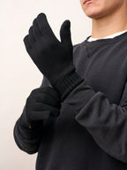 Man in a charcoal sweatshirt pulling on black FibreHeat self-heating merino wool gloves