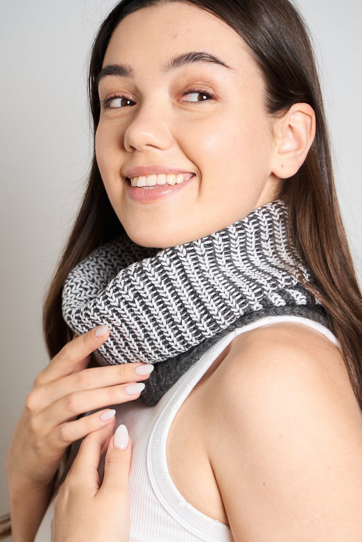 Smiling woman wearing a gray and ecru ribbed self-heating neck warmer