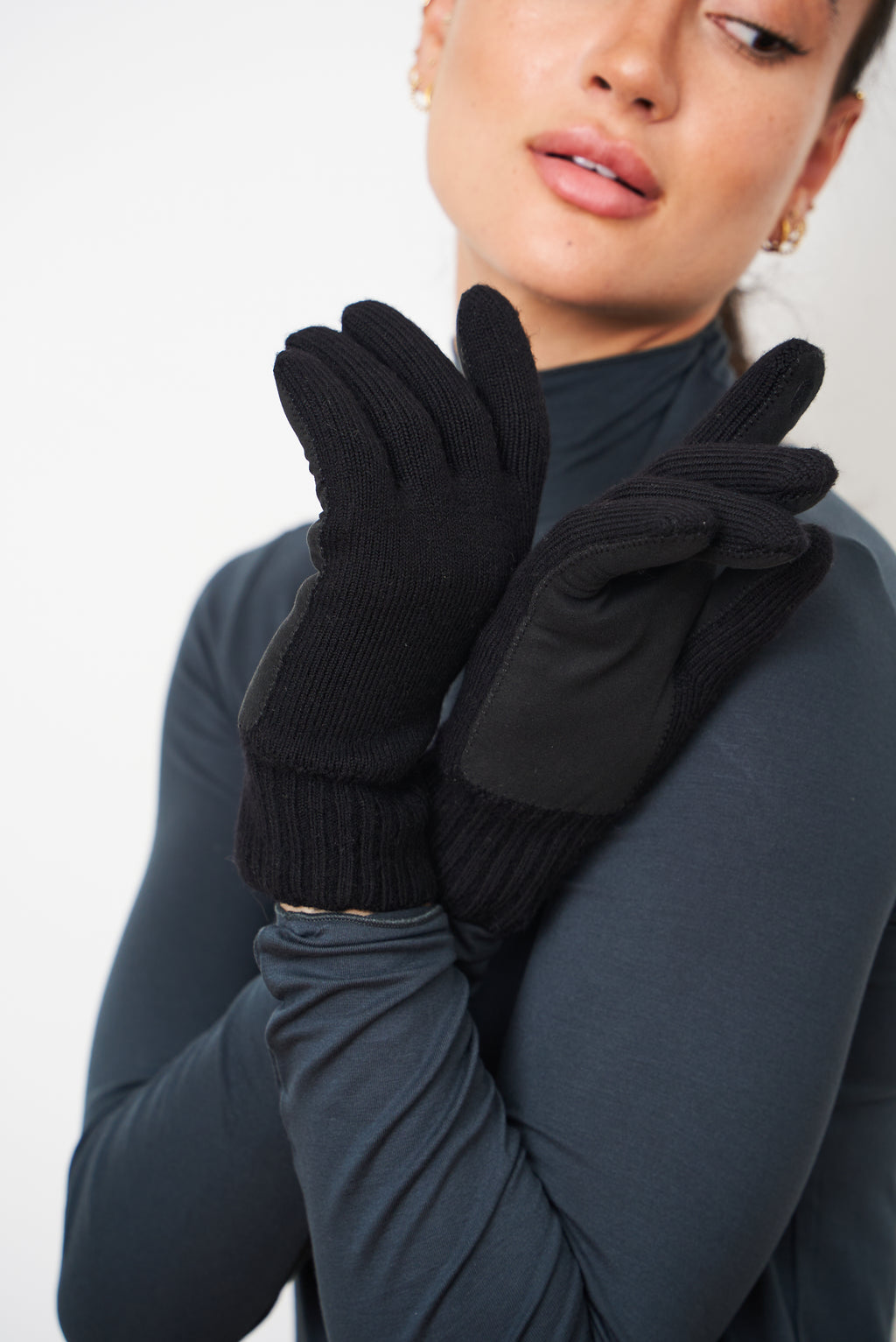 Woman holding her hands near her face, wearing black merino gloves with leather palm patches