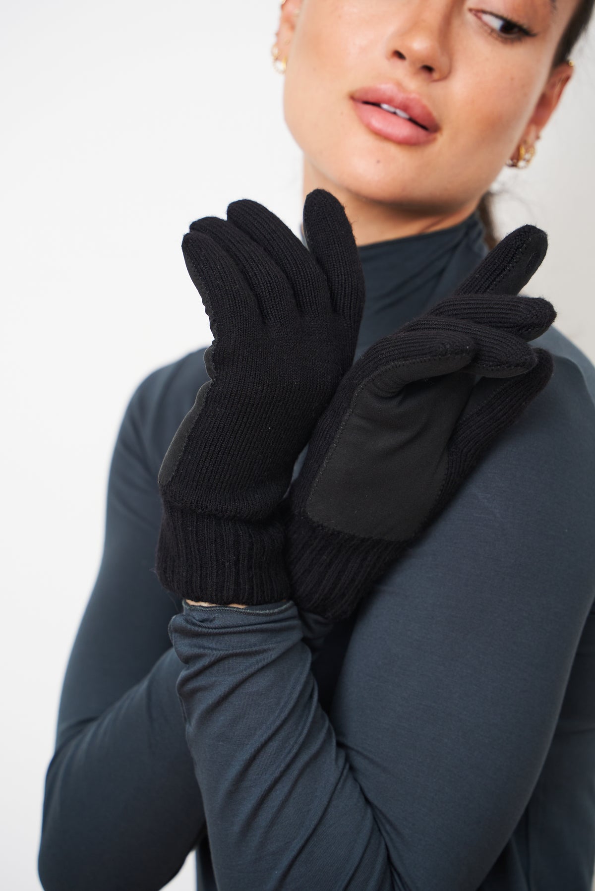 Woman holding her hands near her face, wearing black merino gloves with leather palm patches