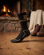 Black and gold FibreHeat Heavy Winter Sock on a cabin floor in front of a stone fireplace