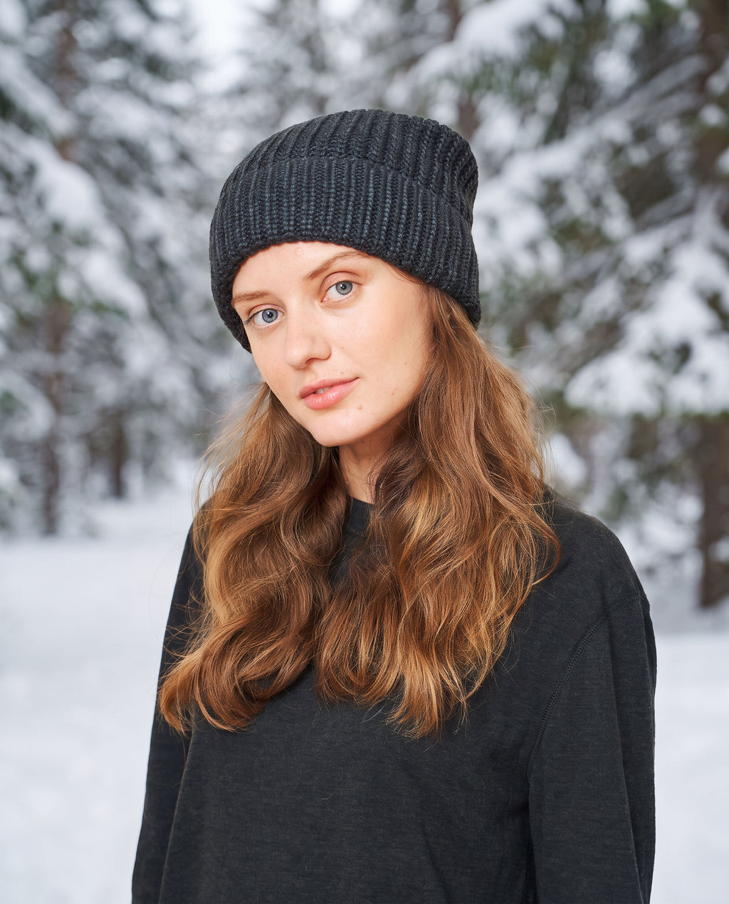 Woman wearing the black FibreHeat knit hat in a snowy pine forest