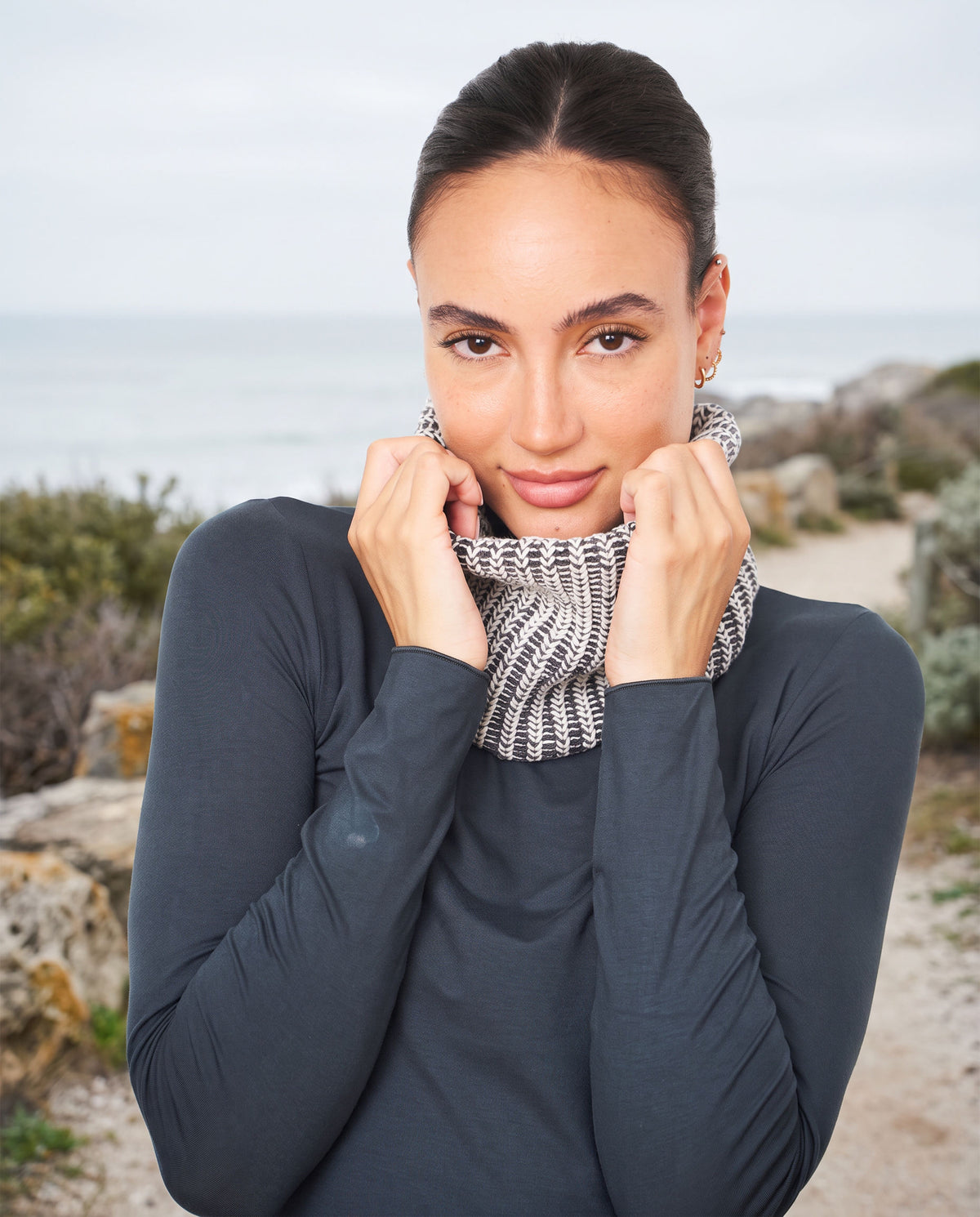 Woman pulling up the gray and ecru FibreHeat neck warmer on a winter coast