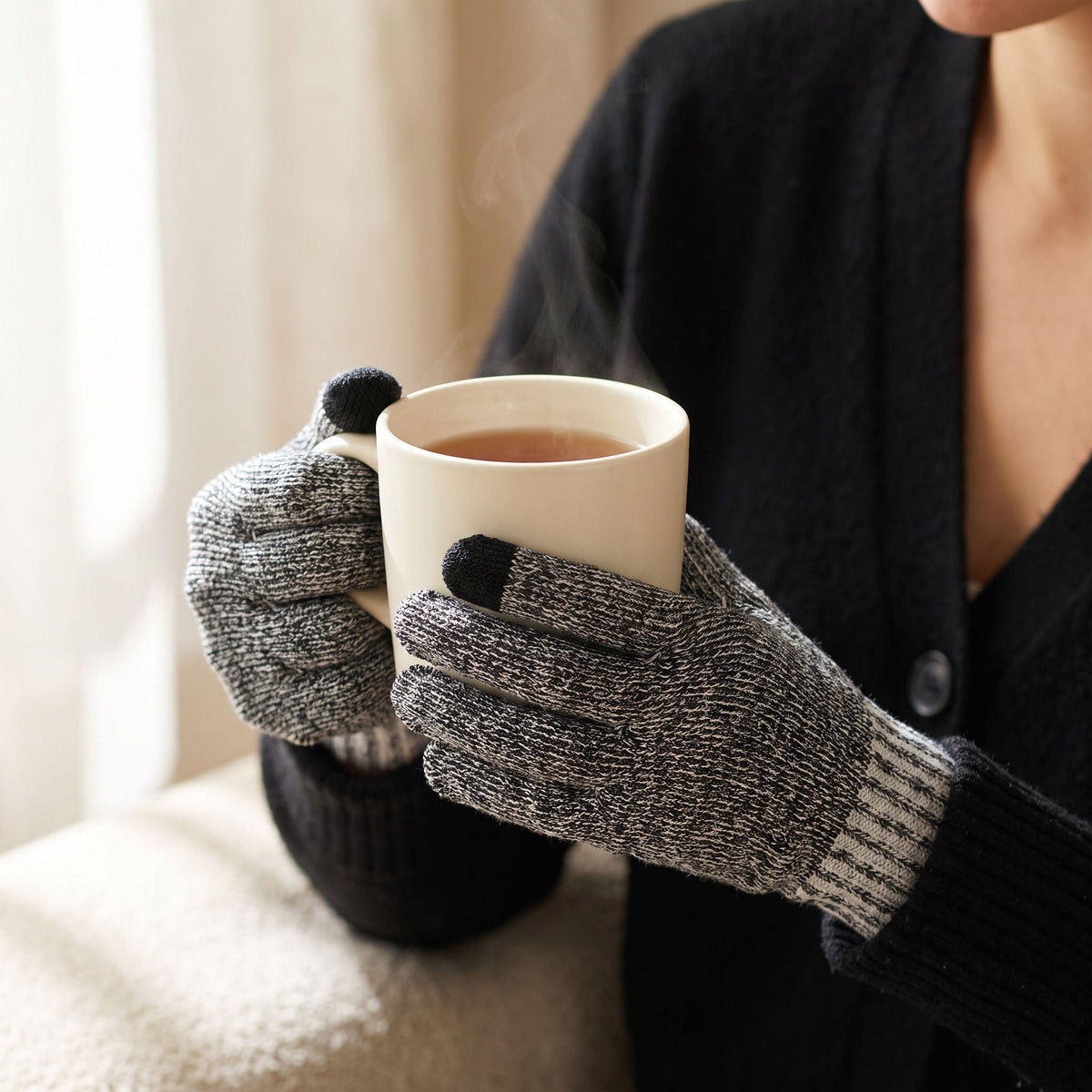 Hands in charcoal twist FibreHeat Ultra Liners wrapped around a warm mug of tea