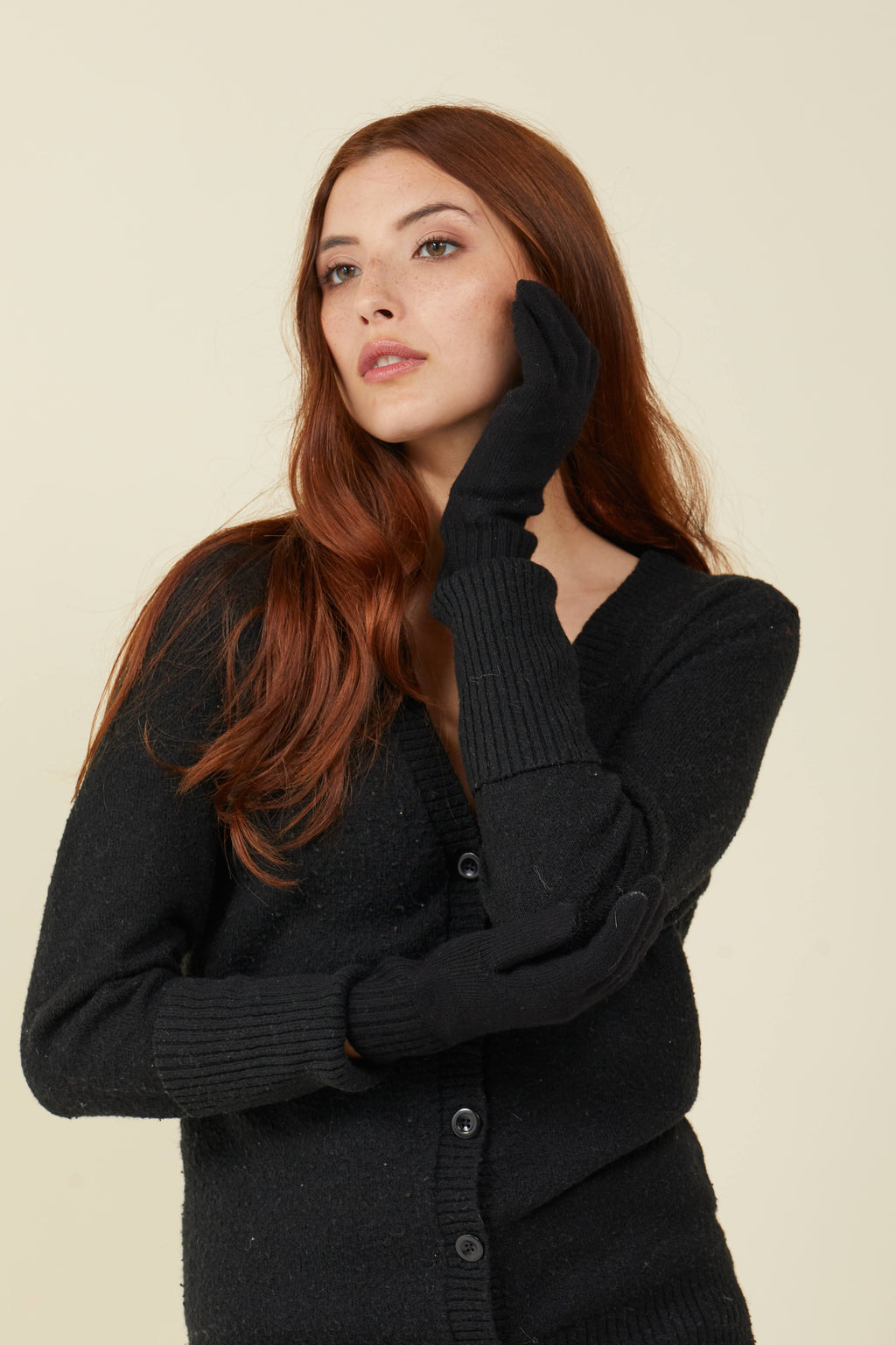 Woman in a black cardigan resting a hand on her cheek, wearing black FibreHeat self-heating merino wool gloves