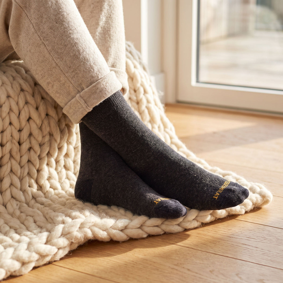 Feet in charcoal FibreHeat Thermal Therapy socks resting on a chunky cream wool throw