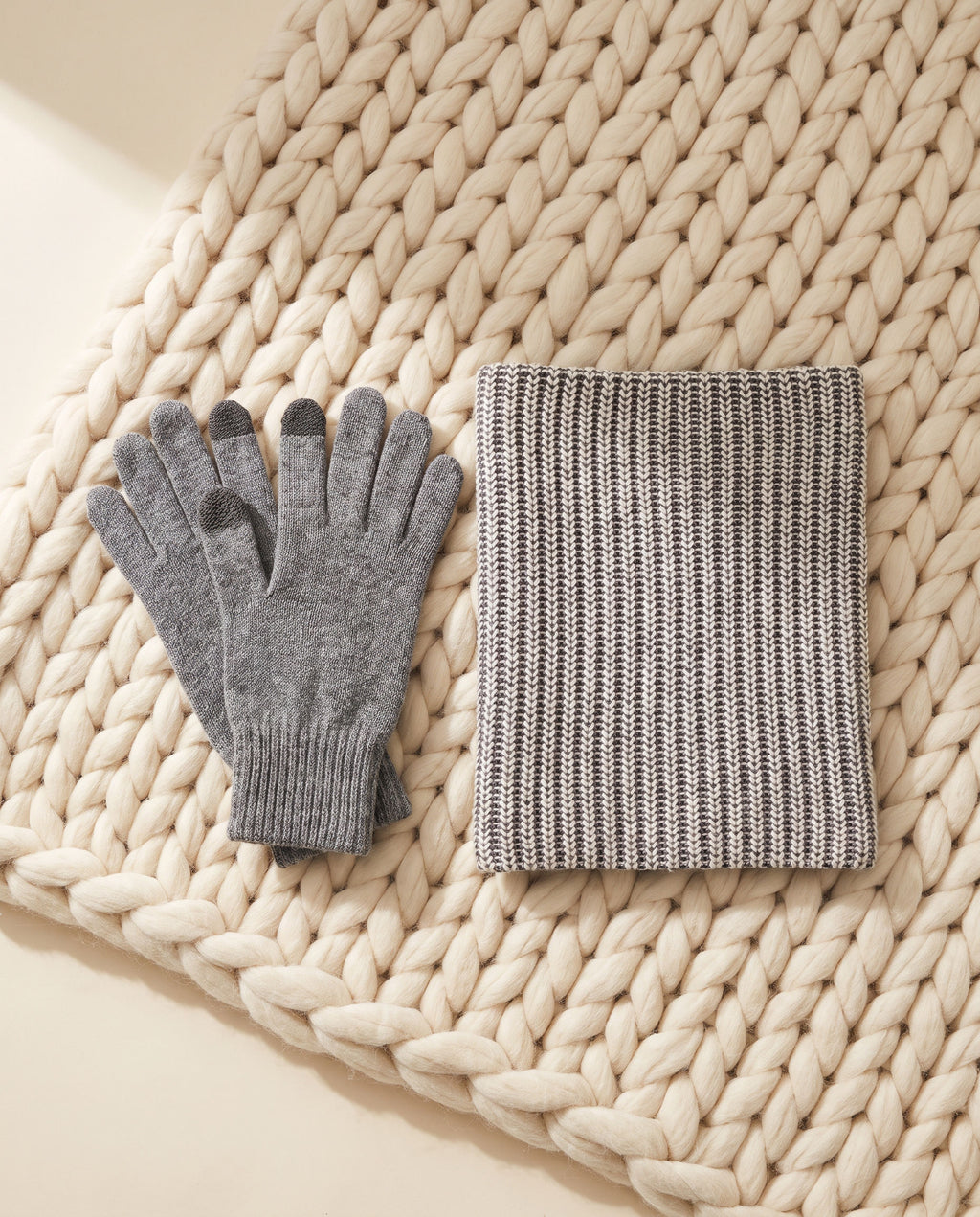 The Cashmere Comfort Set: gray heather cashmere gloves and gray and ecru neck warmer on a cream knit throw